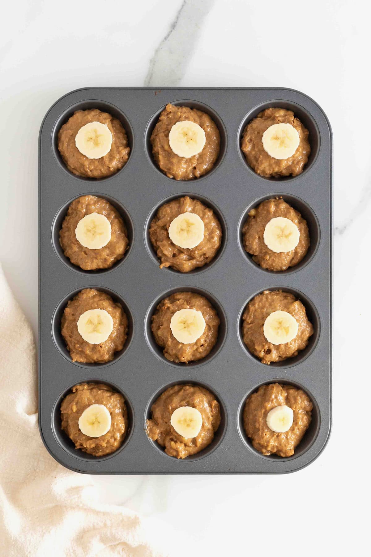 A dark metal muffin tin filled with gingerbread banana muffin batter.