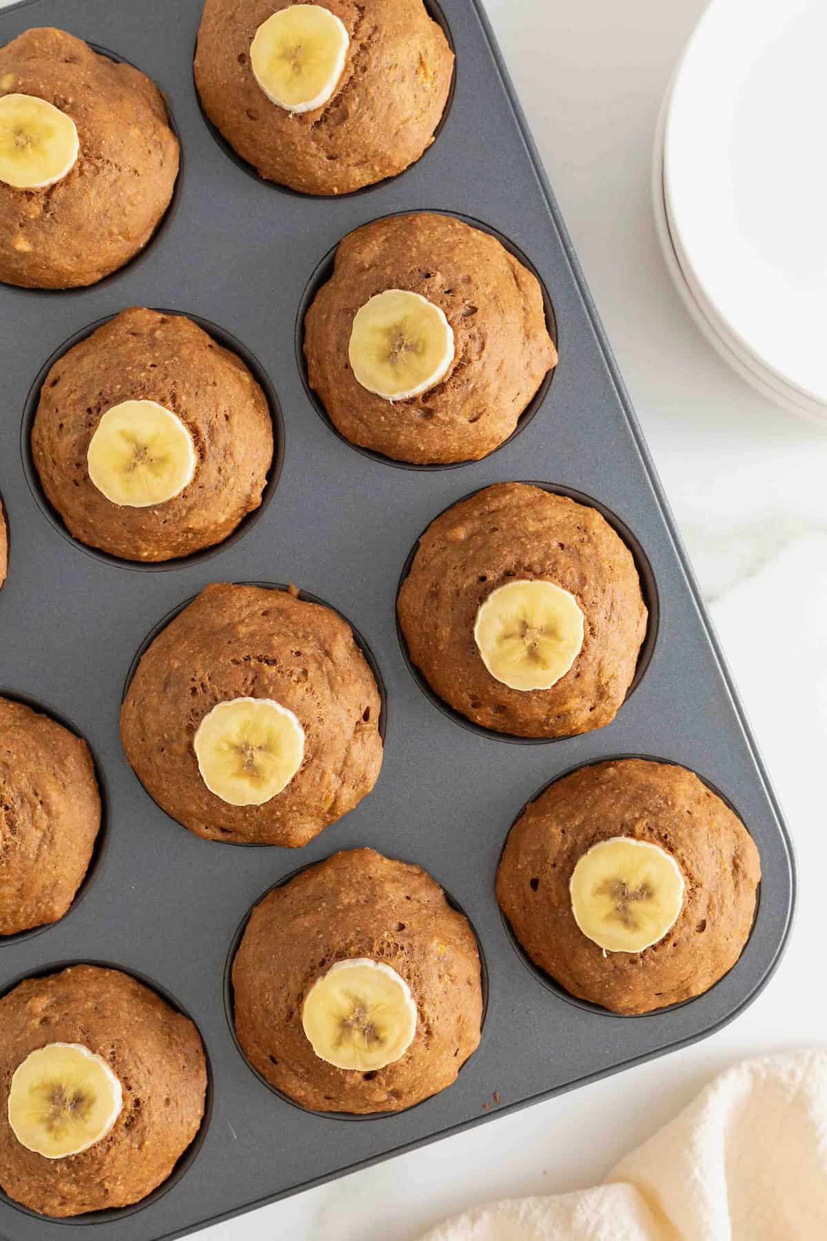 Gingerbread banana muffins garnished with banana slices in a dark metal muffin pan.