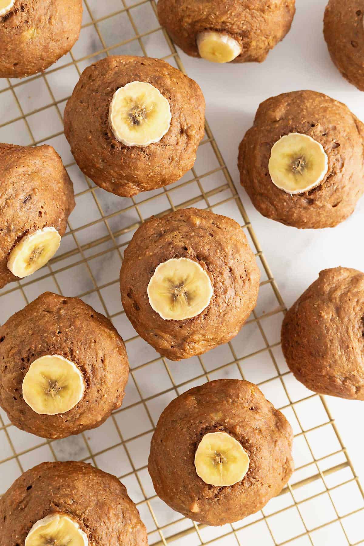 11 gingerbread banana muffins on a gold toned cooling rack over a white surface.