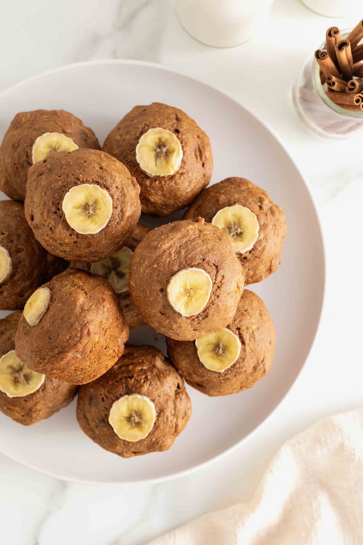 A white serving plate stacked with gingerbread muffins that are garnished with a banana slice.