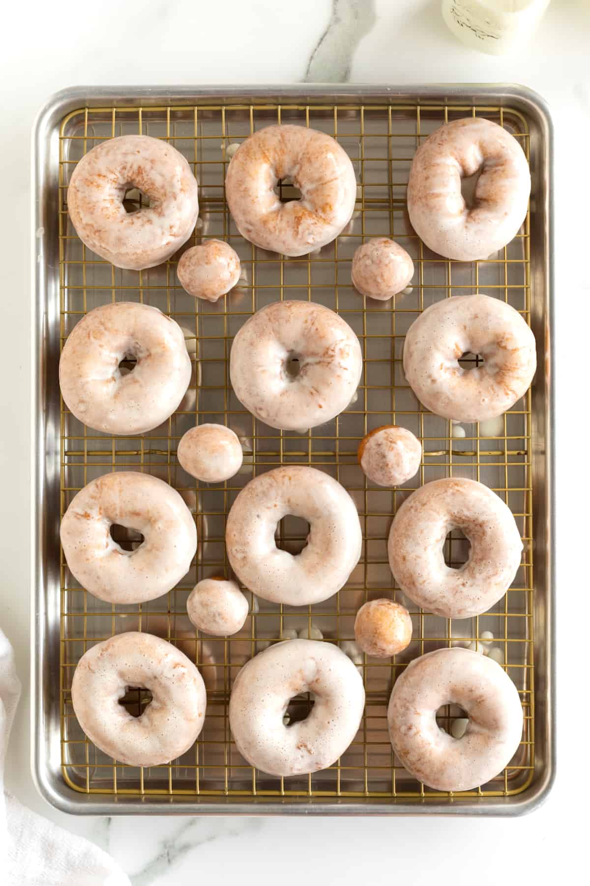 12 glazed donuts and six glazed donut holes on an aluminum baking sheet.
