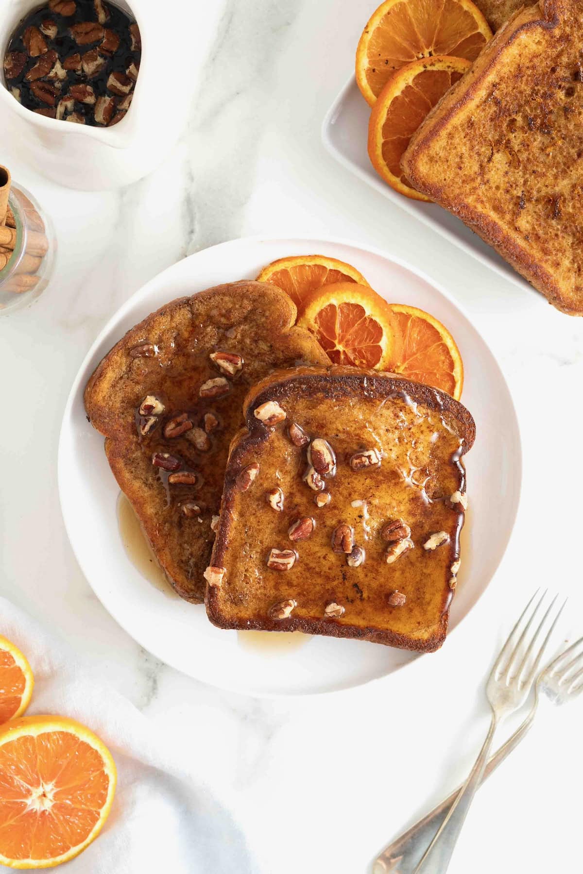 Two slices of orange pecan French toast on a white plate. The plate is garnished with three slices of orange.