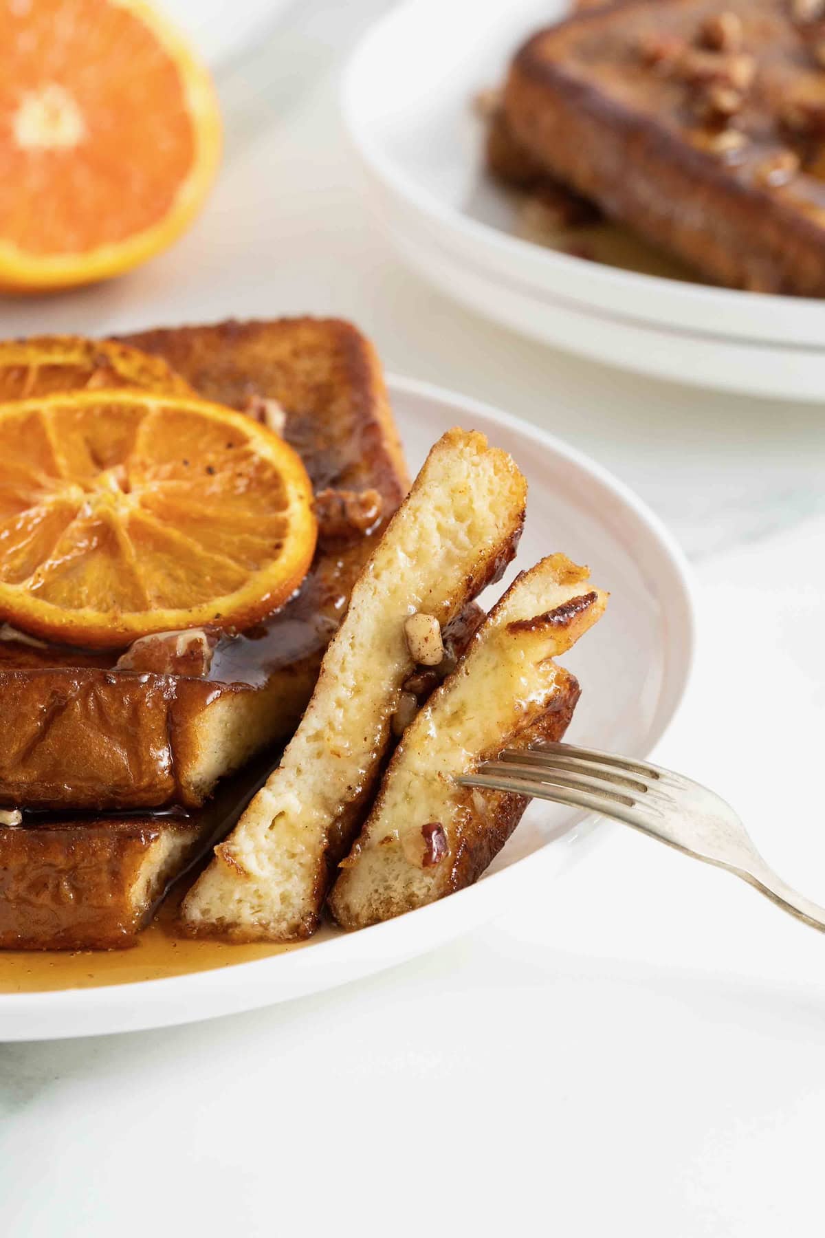 A stack of two pieces of orange pecan French toasts covered in syrup with a bite cut out of it.