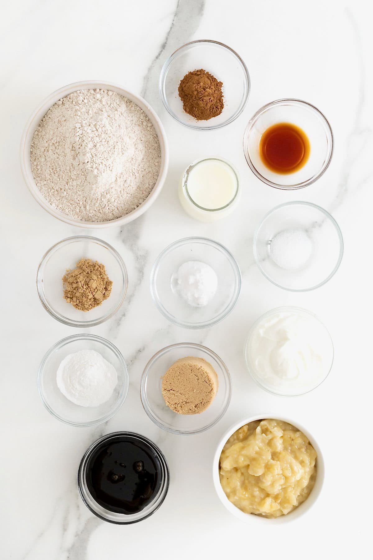 Ingredients for gingerbread banana muffins in small glass dishes on a white marble counter.