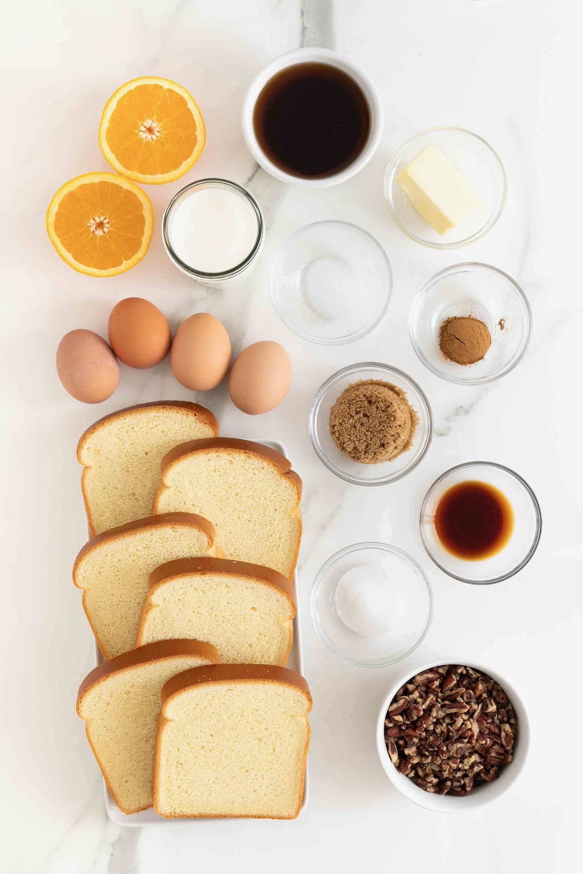 Ingredients to make orange pecan baked French toast in small glass dishes on a white marble counter.