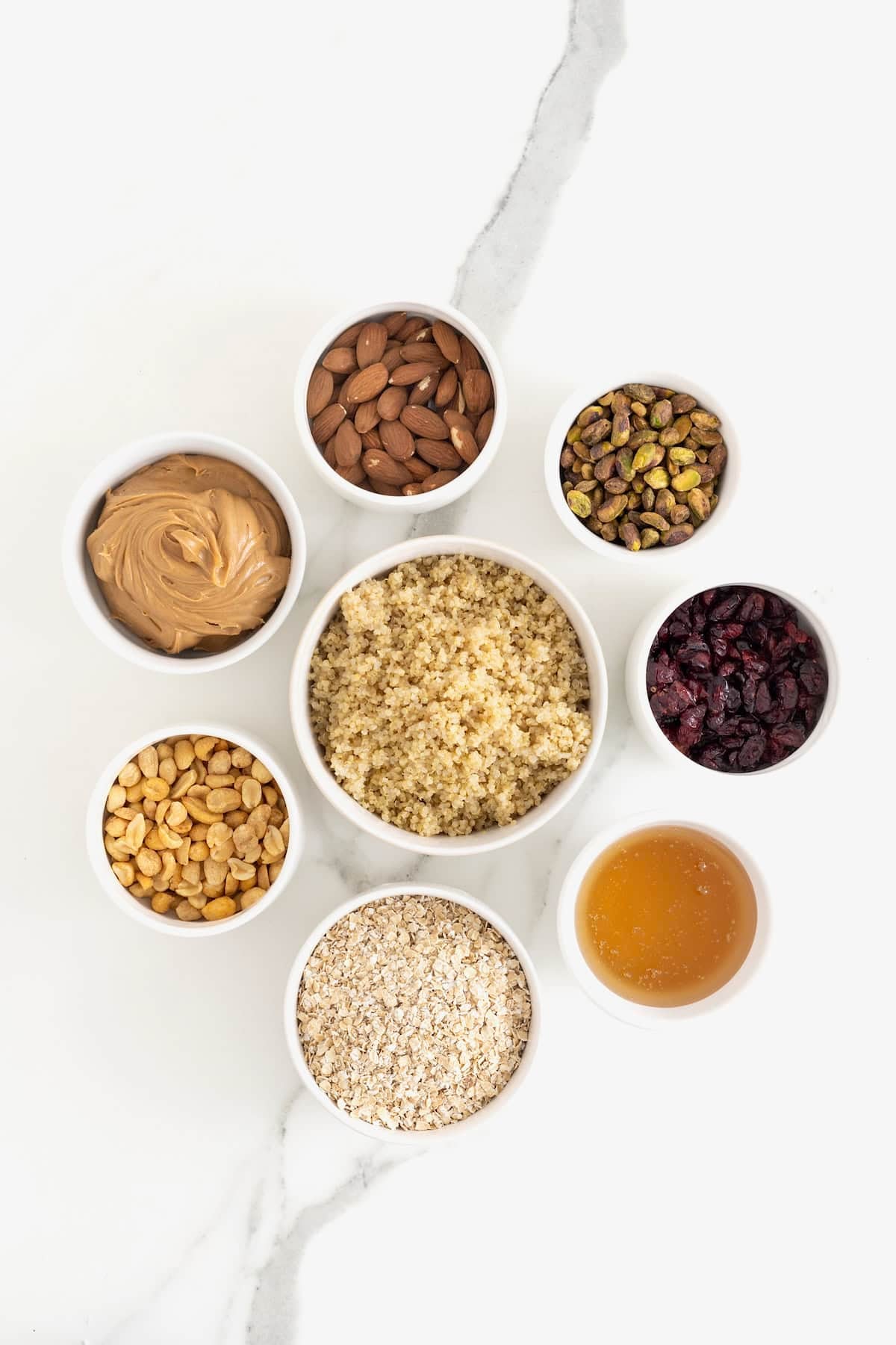 Ingredients to make trail mix quinoa bites in small white dishes on a white marble counter.