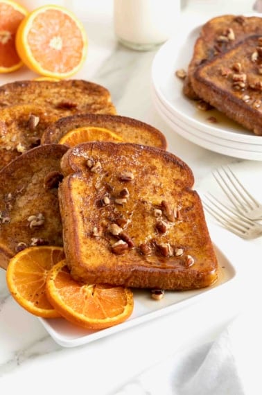 Slices of orange pecan French toast on a white rectangle serving platter.