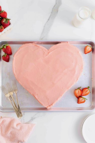 A heart shaped cake with pink icing on a baking sheet.