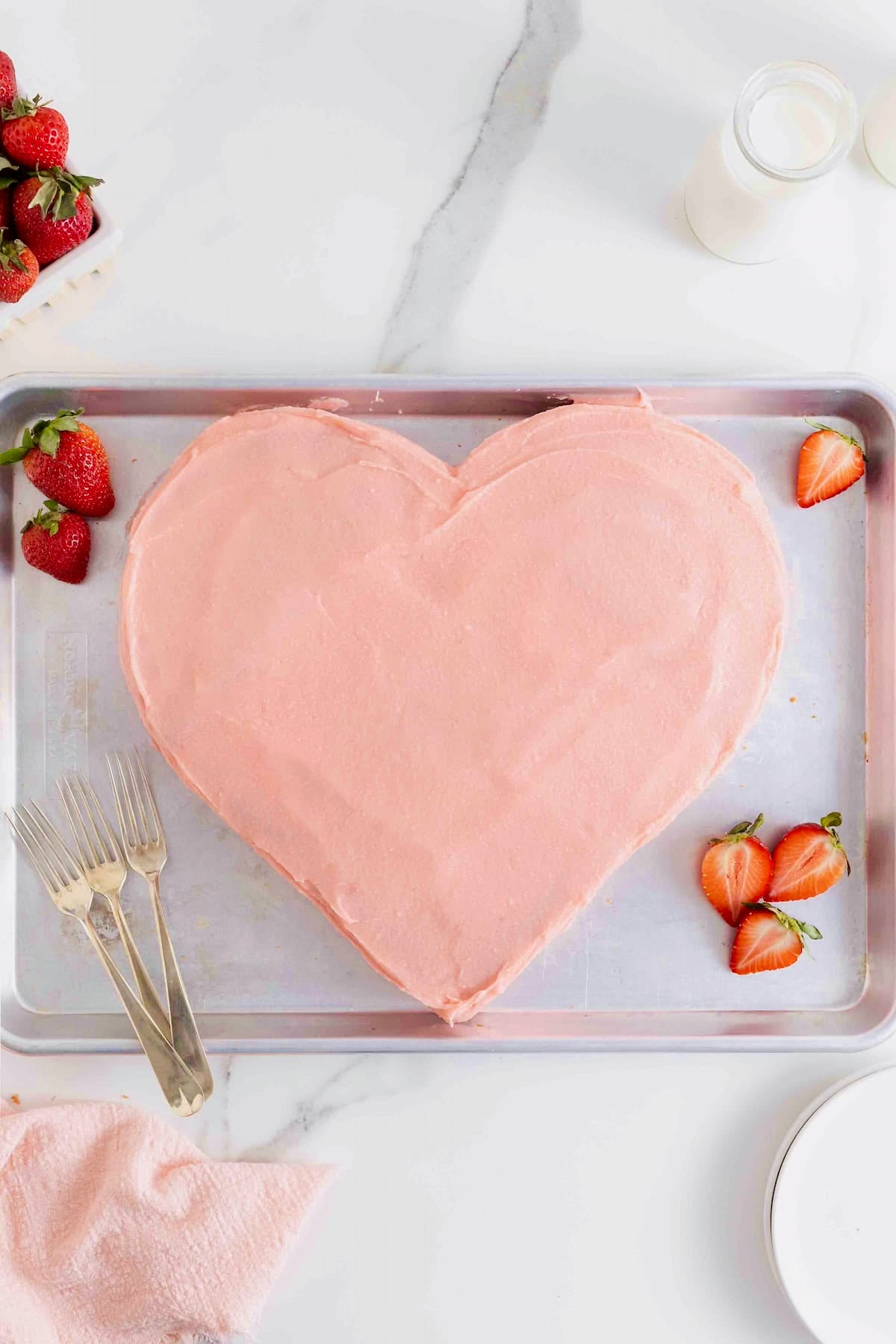 A heart shaped cake with pink icing on a baking sheet.