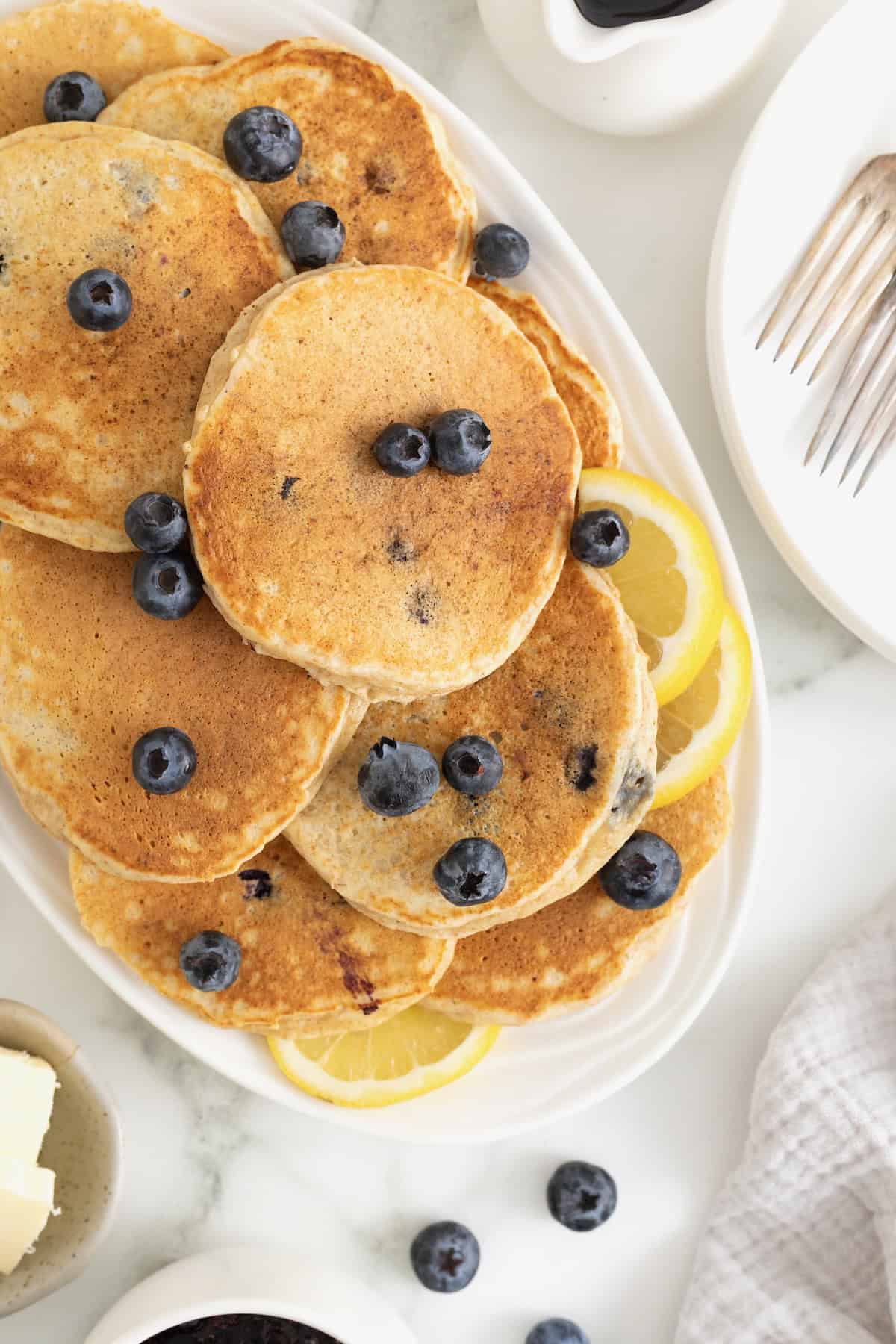A pile of blueberry lemon ricotta pancakes on an oblong white platter.