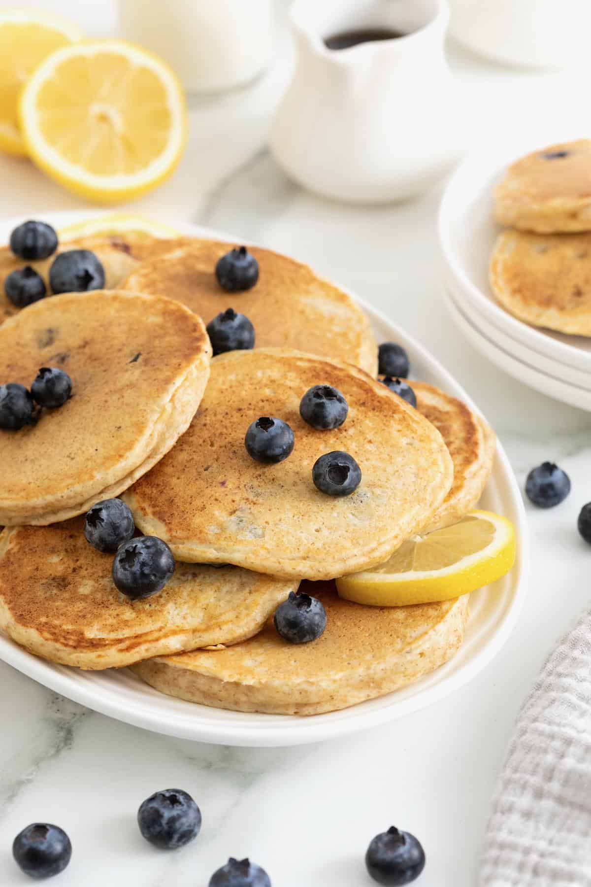A pile of blueberry lemon ricotta pancakes on an oblong white platter.
