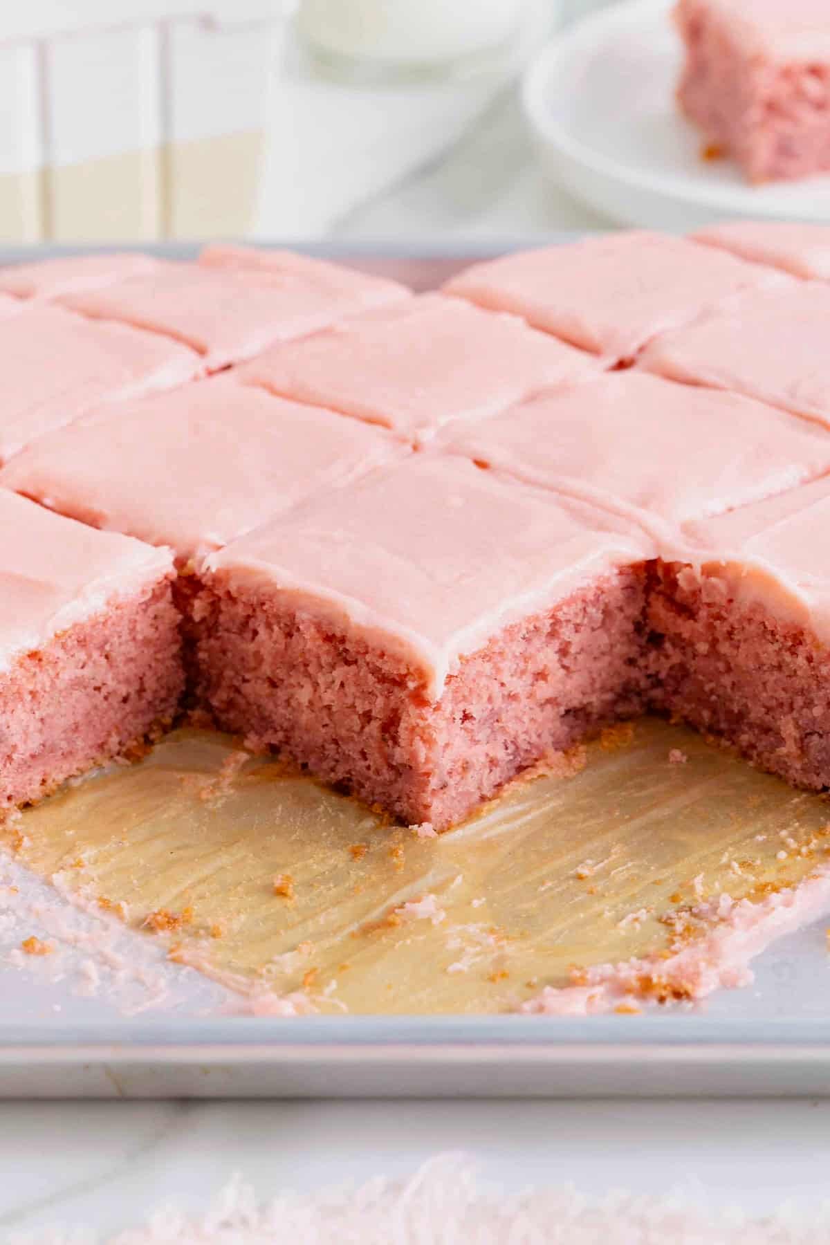 A heart shaped cake with light pink frosting cut into squares.