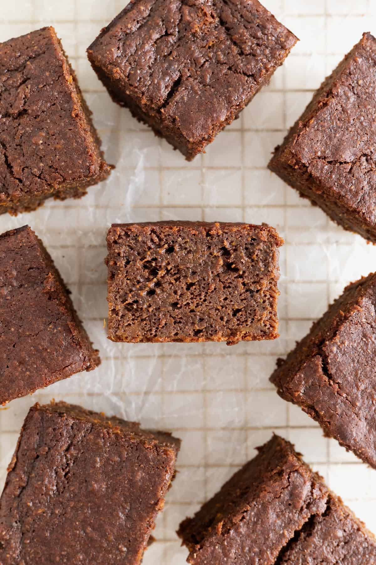Eight whole wheat sweet potato brownies on a parchment lined gold toned cooling rack.