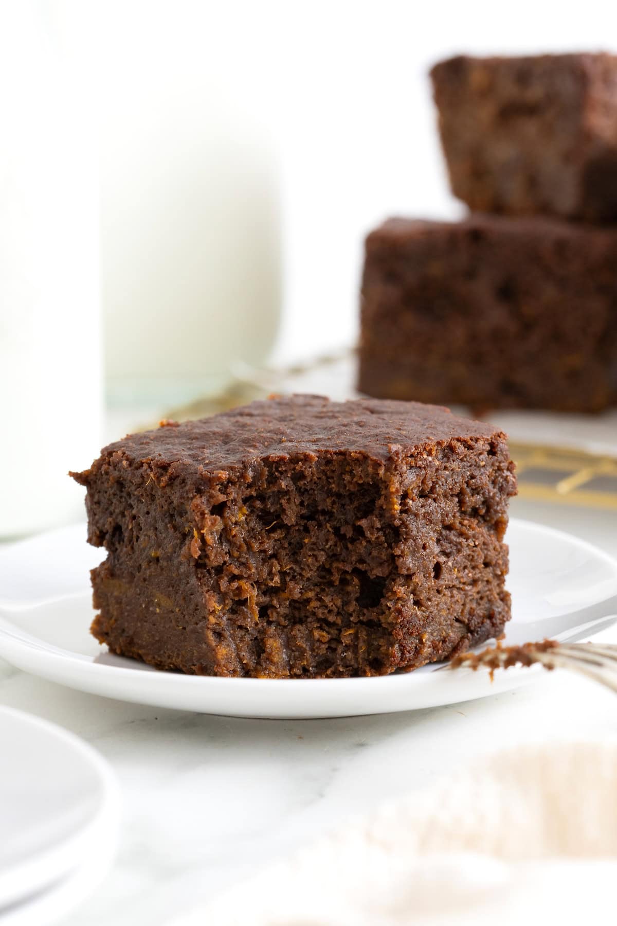 A whole wheat sweet potato brownie with a bite taken out of it on a white plate.