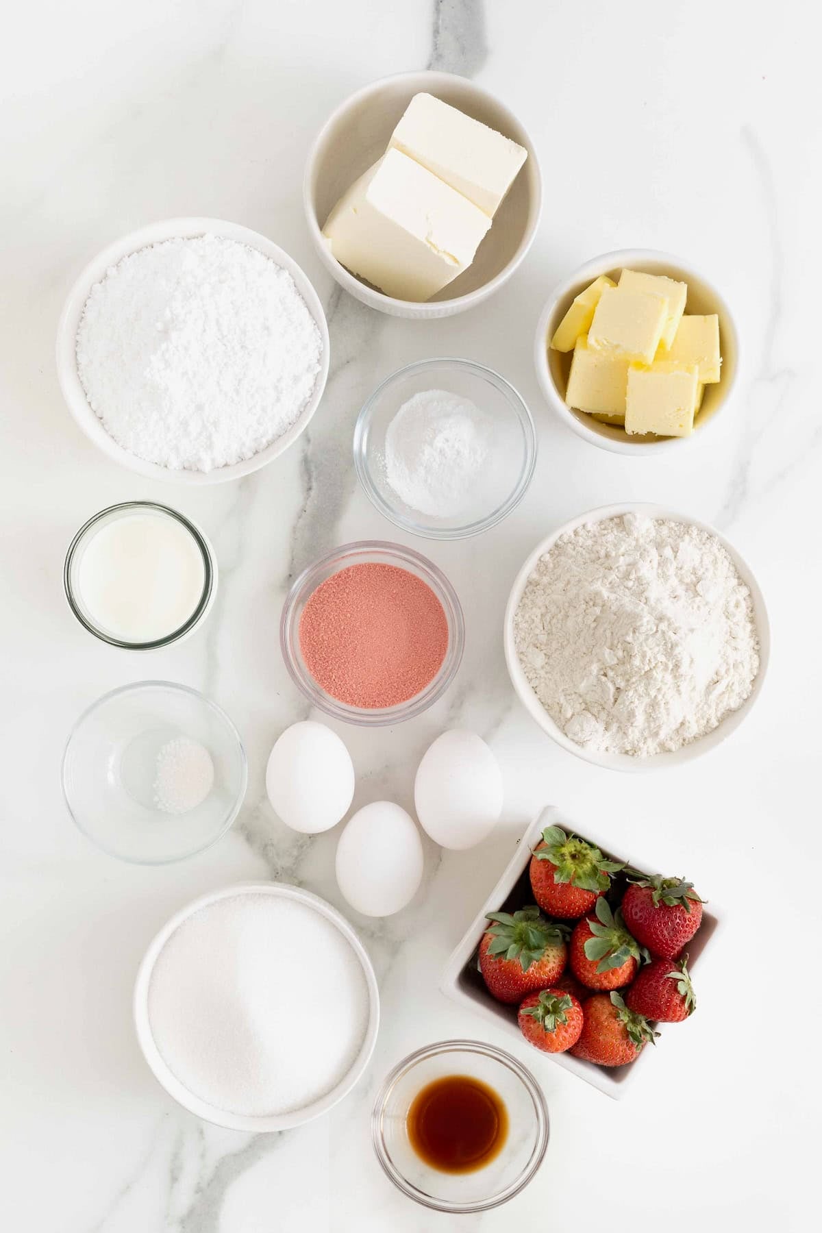 Ingredients to make fresh strawberry heart cake in small glass bowls on a white marble counter.