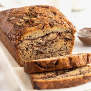 A loaf of Nutella swirled banana bread on a rectangular white serving platter. The bread is sliced, revealing the swirls of Nutella inside.