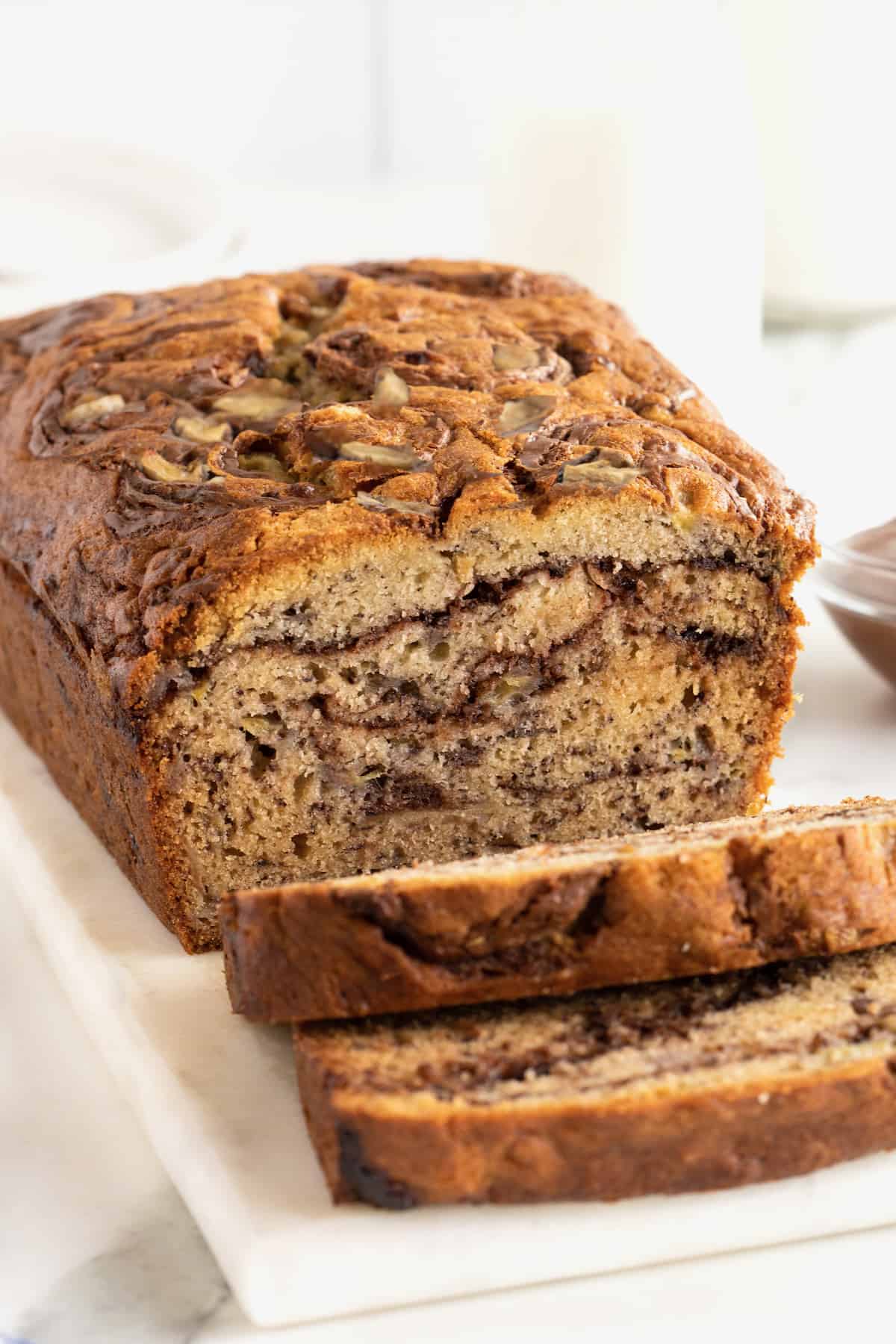 A loaf of Nutella swirled banana bread on a rectangular white serving platter. The bread is sliced, revealing the swirls of Nutella inside.