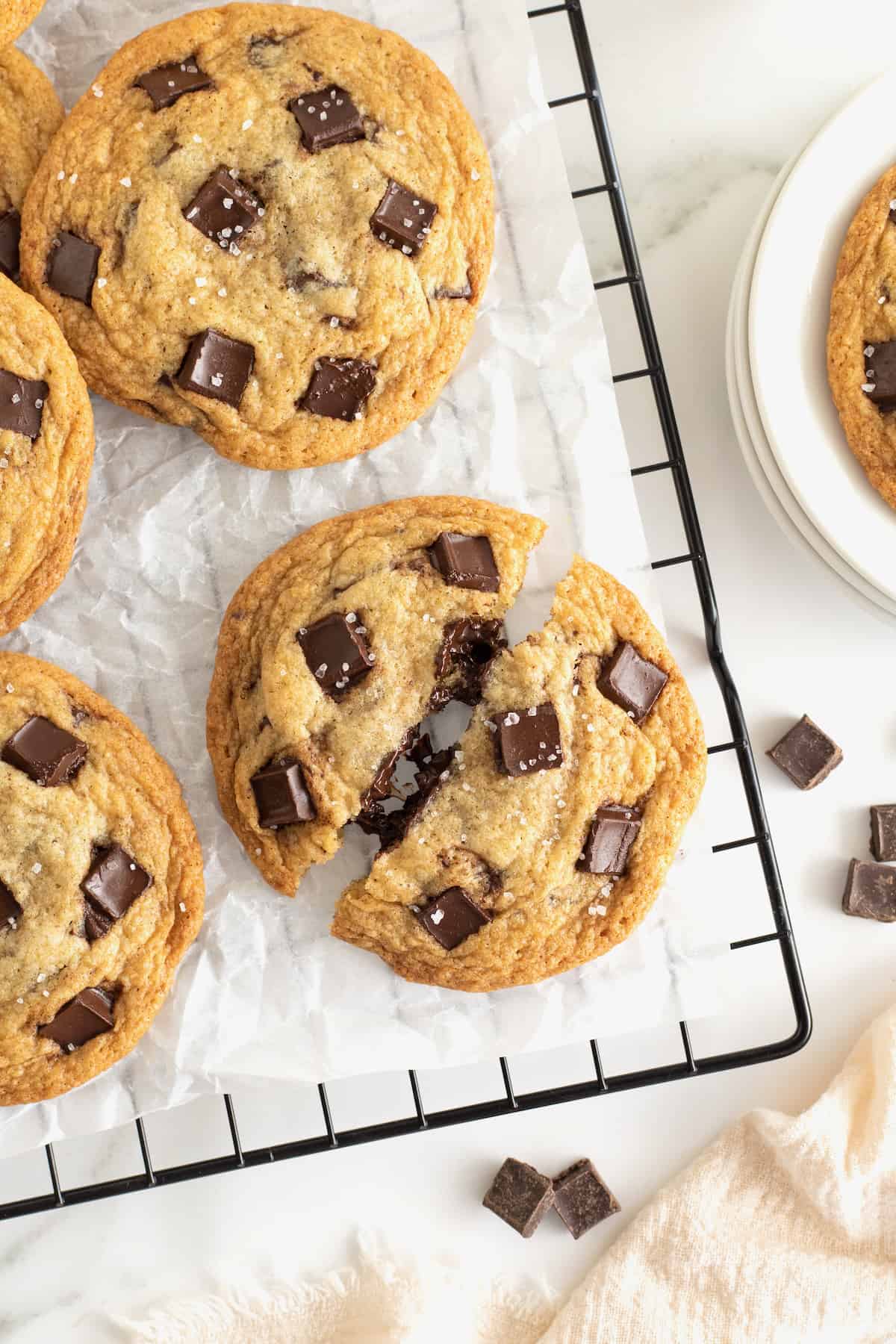 A parchment lined cooling rack with cookies filled with chocolate chunks and sprinkled with sea salt.
