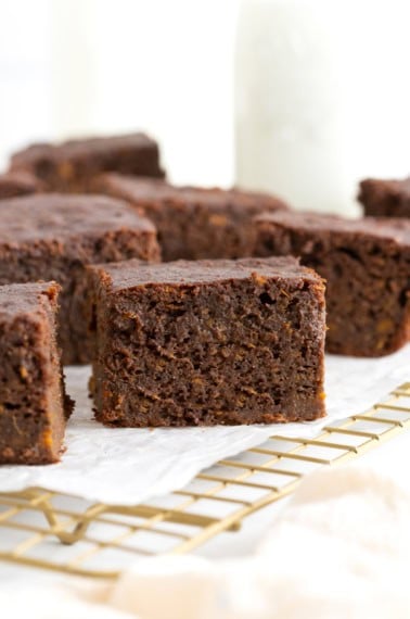Seven whole wheat sweet potato brownies on a parchment lined gold toned cooling rack.