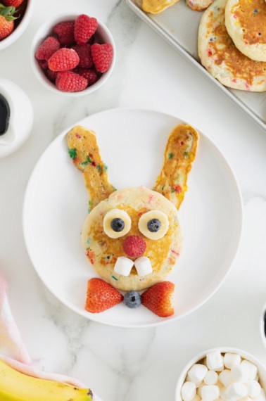 A white plate with pancakes made to look like the Easter bunny, with a strawberry bowtie.