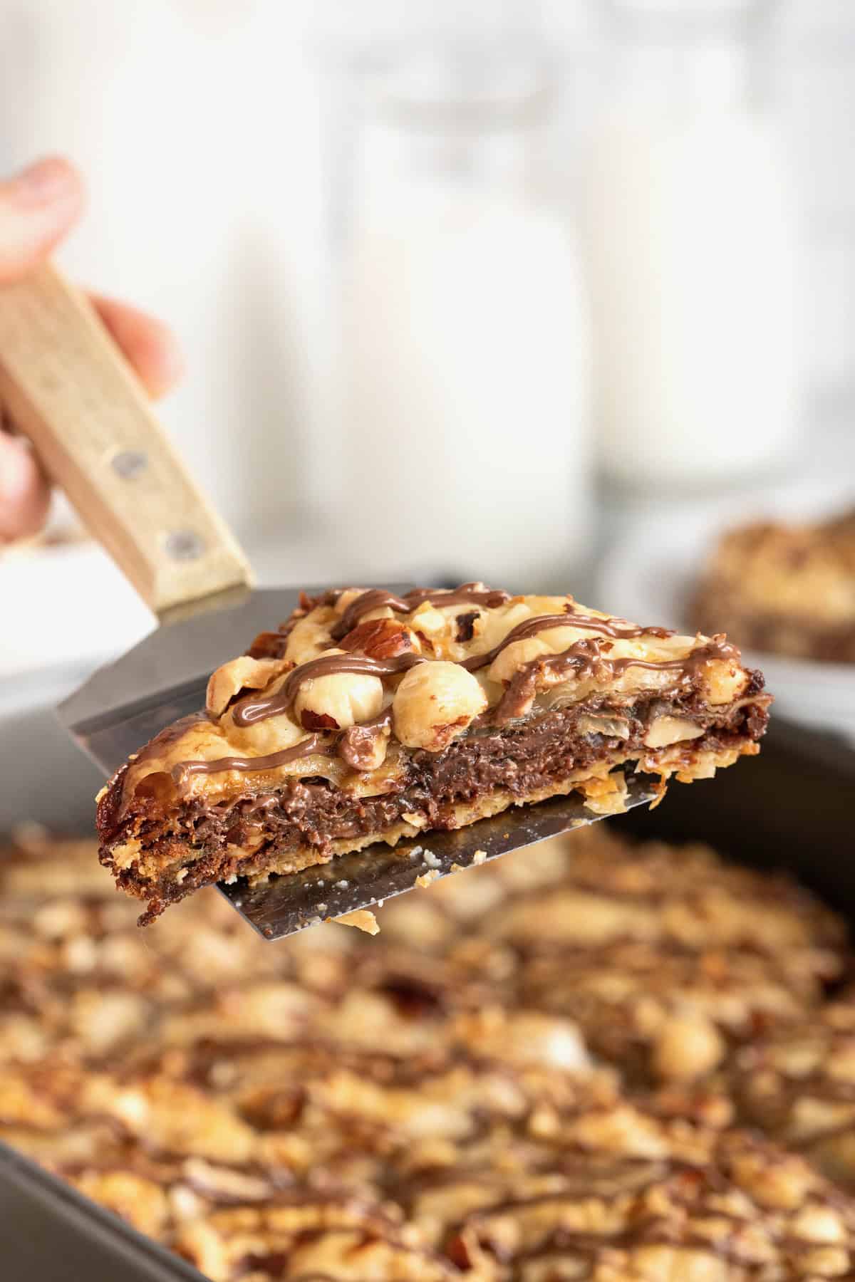 A piece of Nutella baklava being lifted from a baking pan using a wood handled spatula.