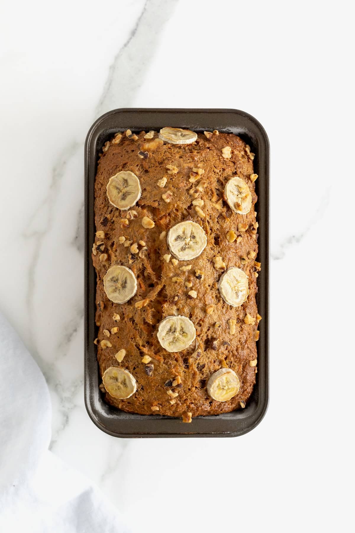 A loaf of whole wheat banana nut carrot cake bread in a dark metal loaf pan.