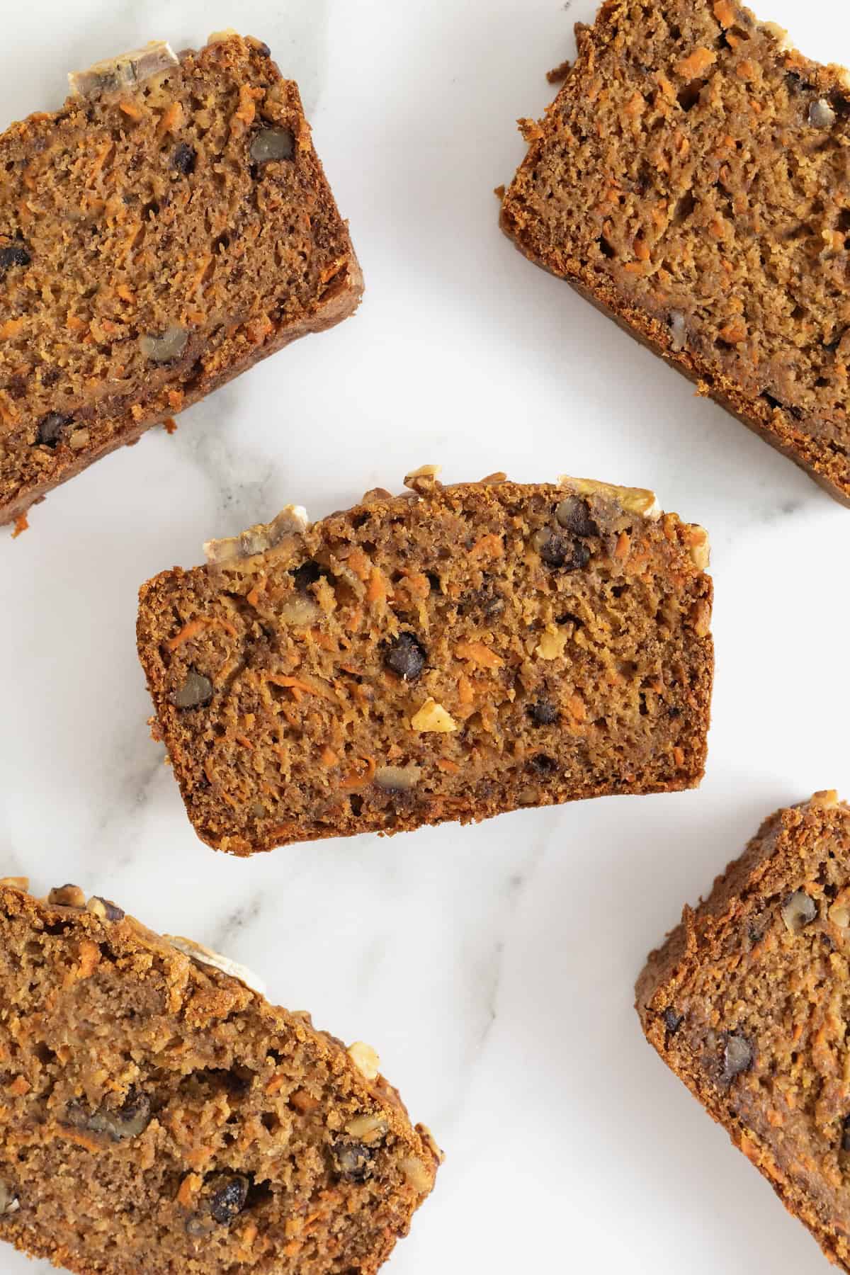 Five slices of banana nut carrot cake bread on a white marble counter.