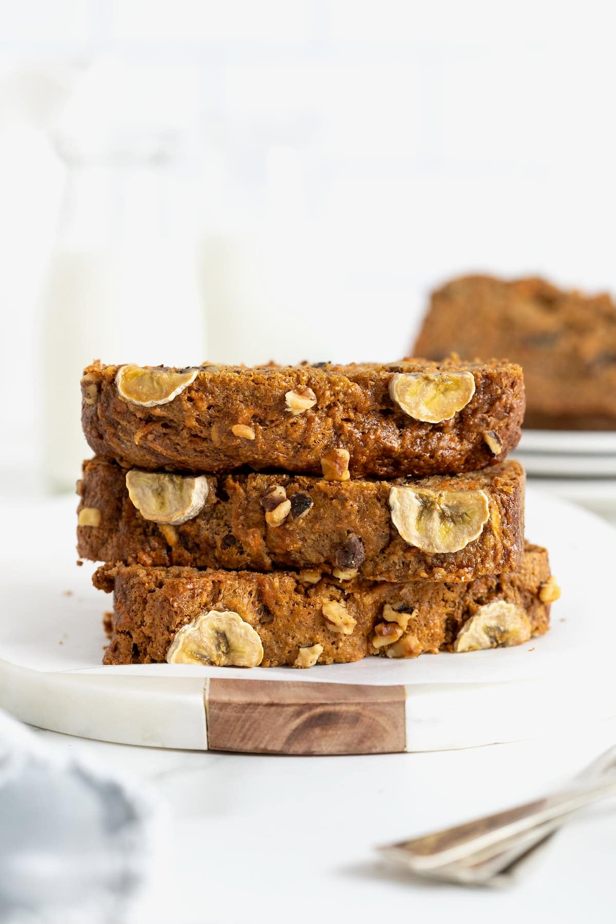 A stack of three slices of banana nut carrot cake bread on a white cutting board.