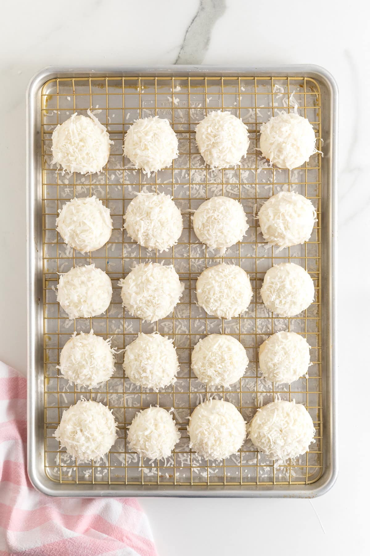 20 white chocolate dipped coconut cookies on a wire cooling rack over an aluminum baking sheet.