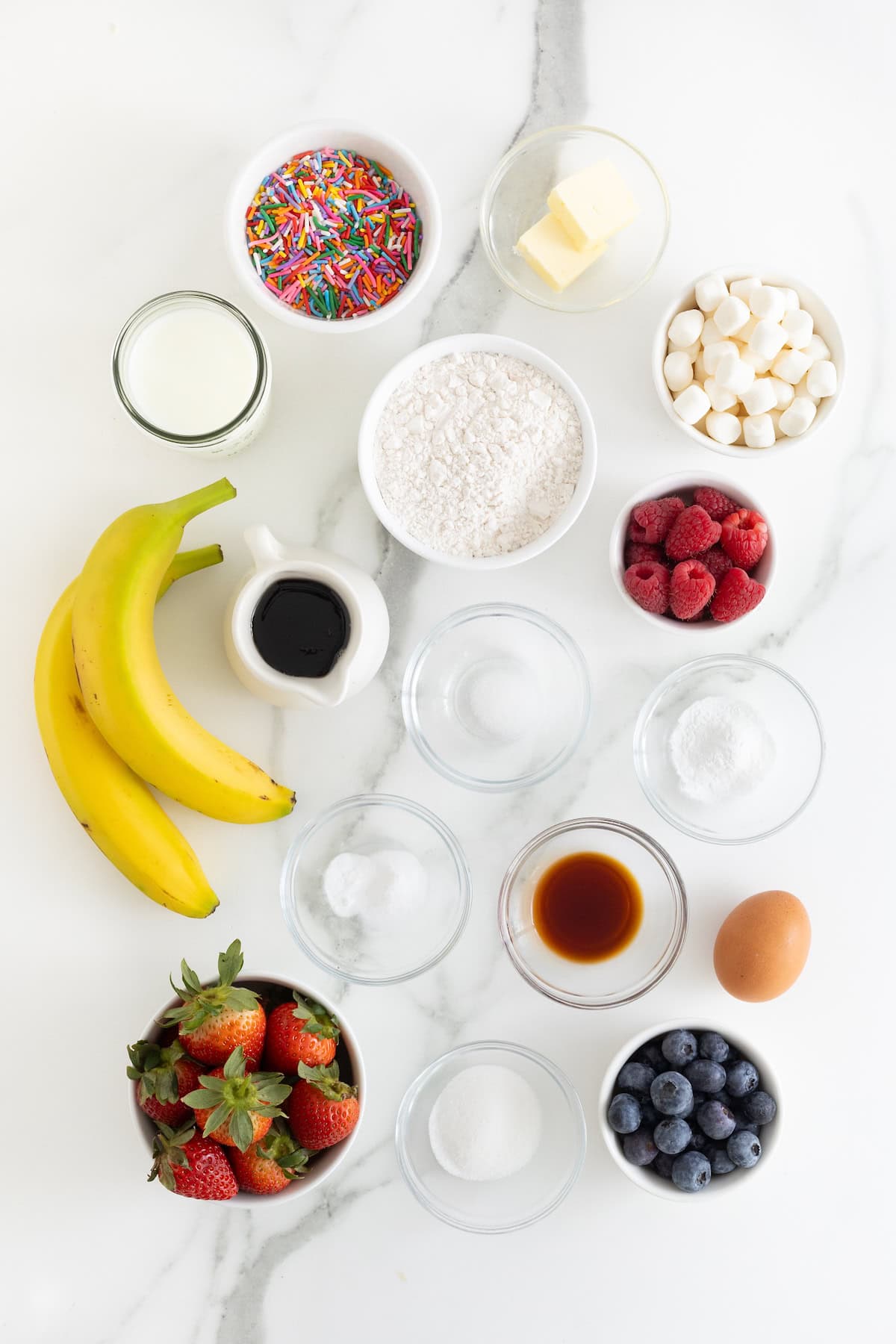Ingredients to make bunny shaped pancakes in small glass dishes on a white marble counter.