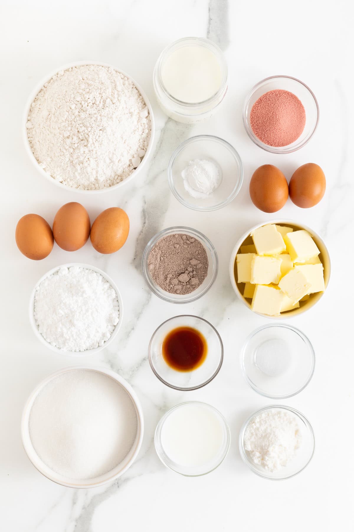 Ingredients to make Neapolitan pound cake in small glass dishes on a white marble counter.