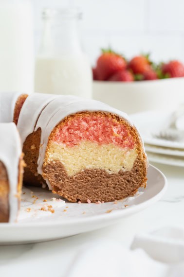 A Neapolitan pound cake with a slice cut out of it revealing layers of pink, white and brown.