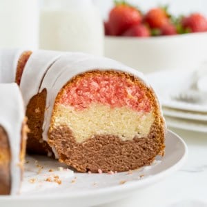 A Neapolitan pound cake with a slice cut out of it revealing layers of pink, white and brown.