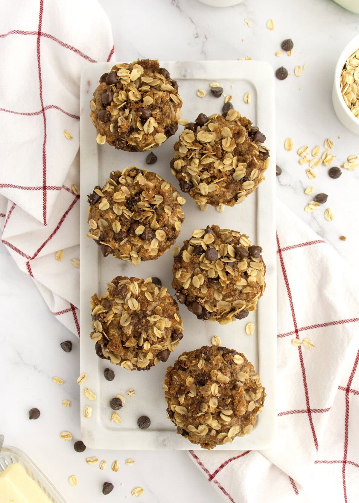 Six oatmeal chocolate chip muffins on a white stone cutting board.
