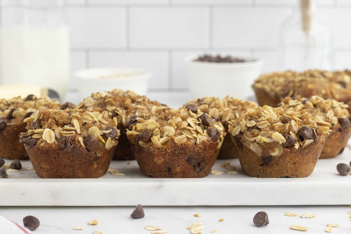Six oatmeal chocolate chip muffins on a white stone cutting board.