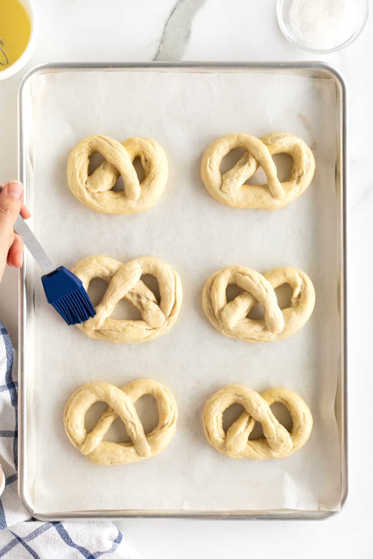 Six uncooked soft pretzels on a parchment lined baking sheet.