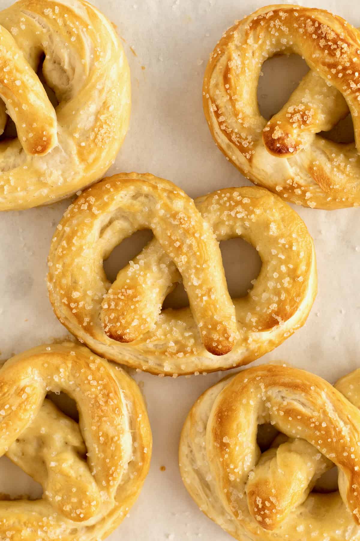 A close up of five homemade pretzels on a sheet of parchment paper.