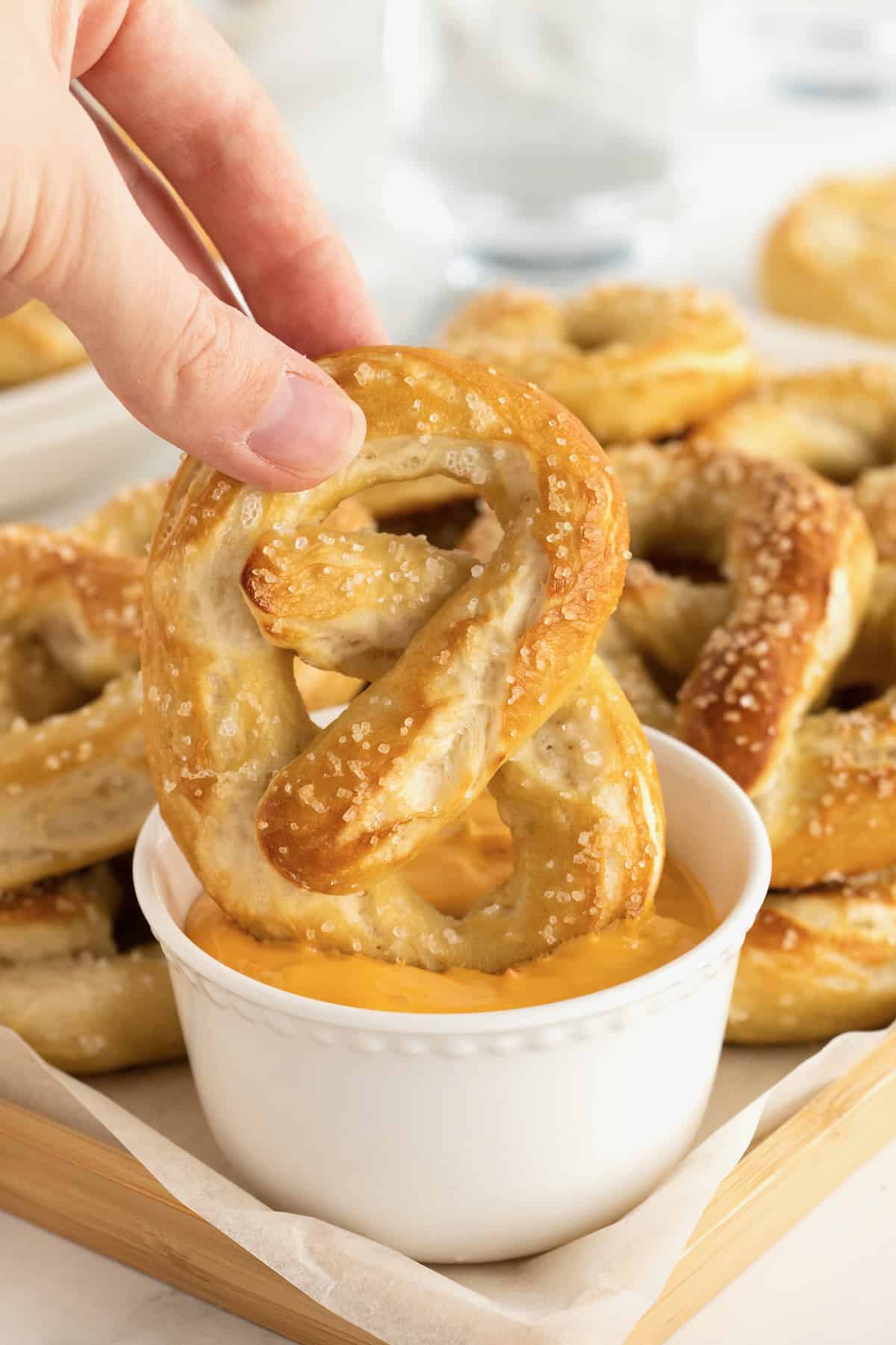 A hand dipping a soft pretzel into cheese sauce.