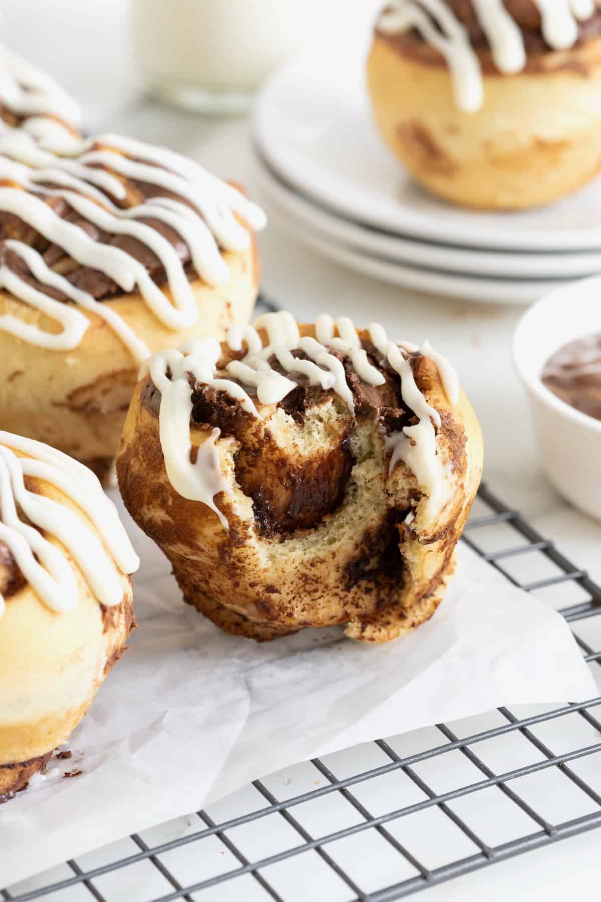 Three Nutella roll muffins on a parchment lined cooling rack. The foremost muffin has a bite out of it revealing layers of Nutella.