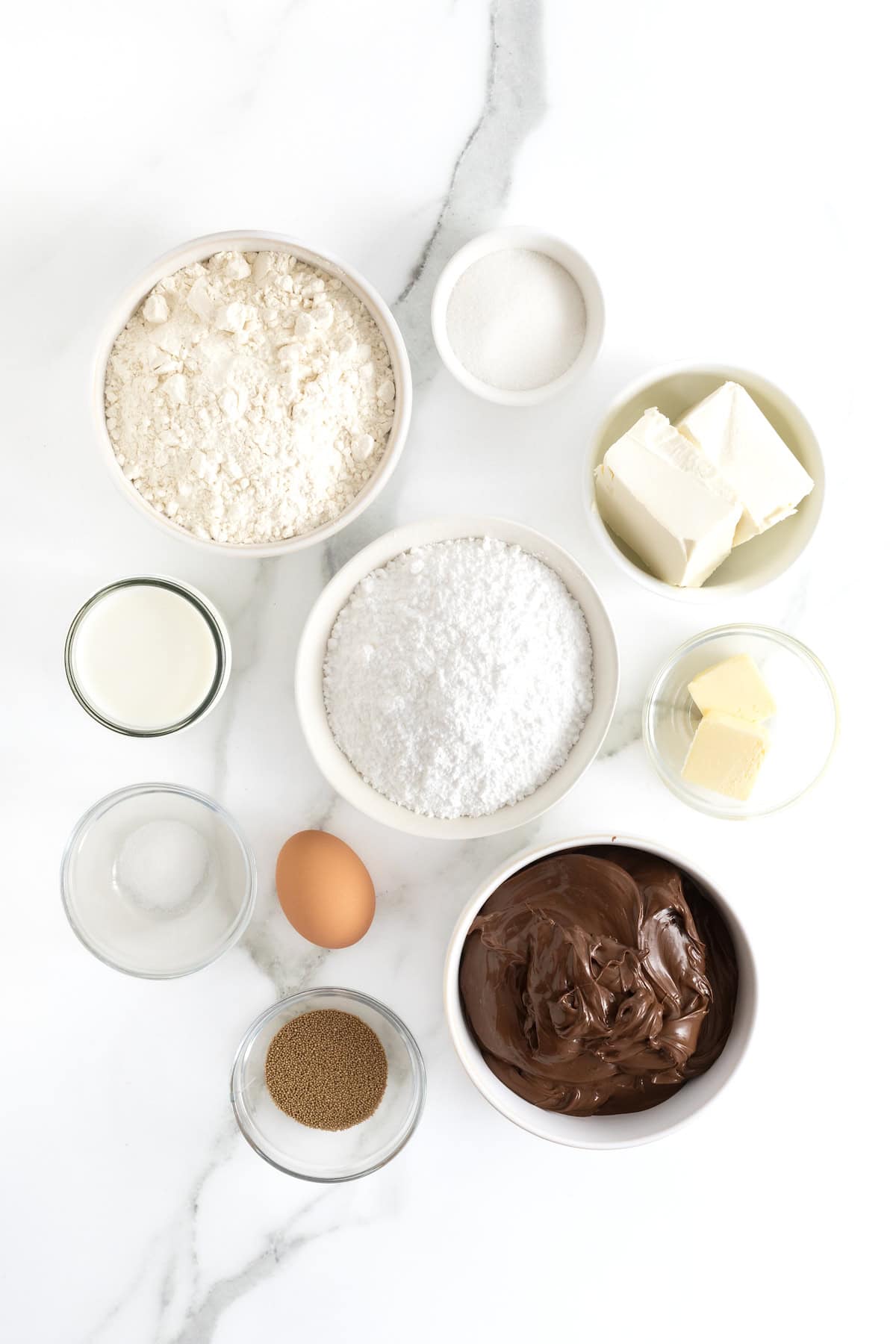 Ingredients to make Nutella Roll Muffins in small glass dishes on a white marble counter.