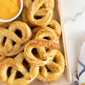 A wooden tray filled with soft pretzels and a small white dish of cheese sauce.