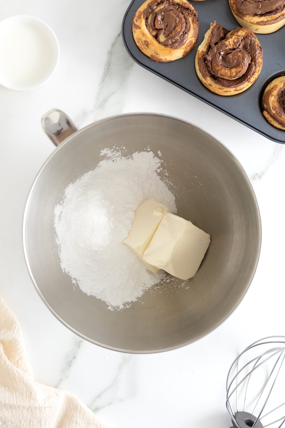 Cream cheese and powdered sugar in the bowl of a stainless steel mixer.