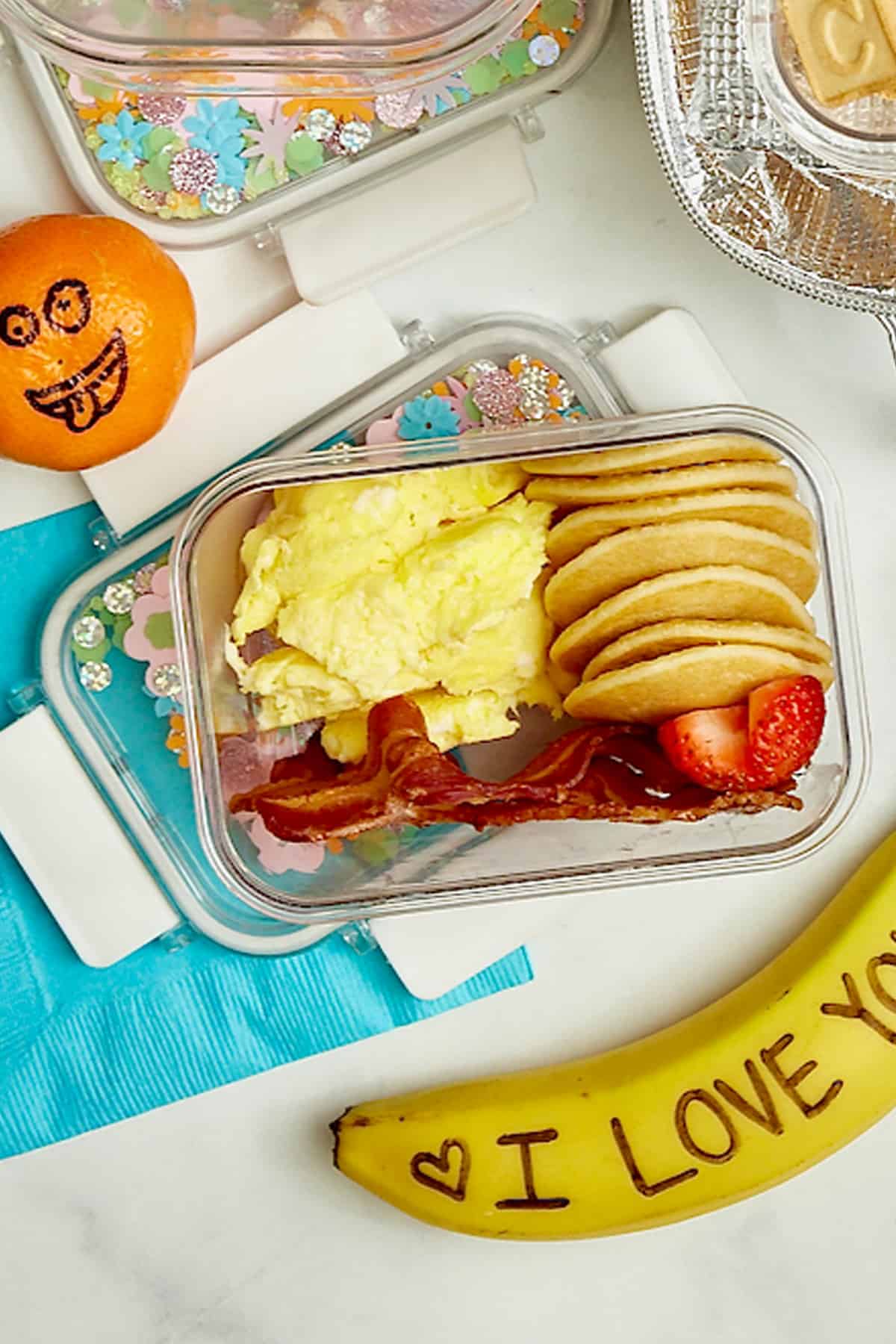 Mini pancakes, scrambled eggs and sliced strawberries in a lunch box.
