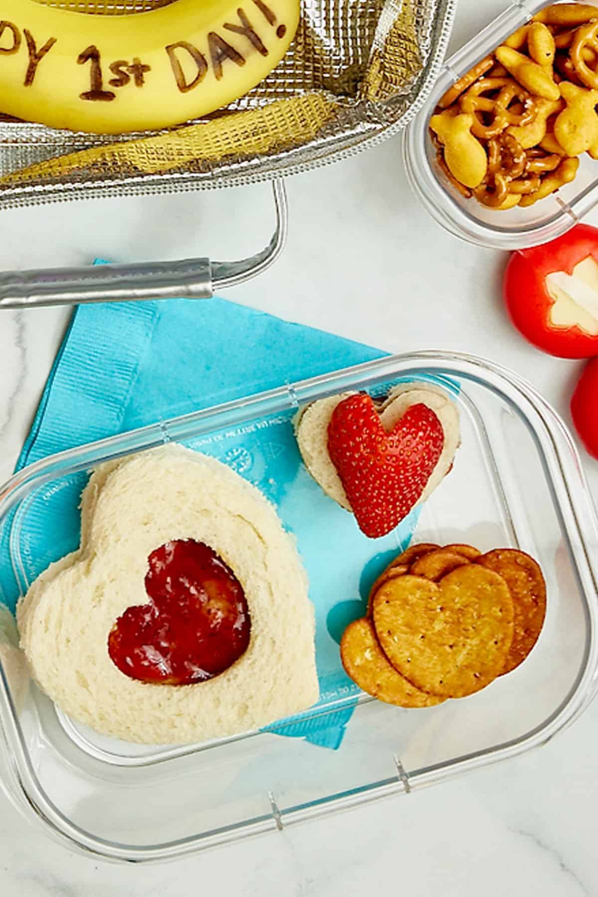 A lunch container with a heart sandwich, heart crackers, and a heart shaped strawberry.