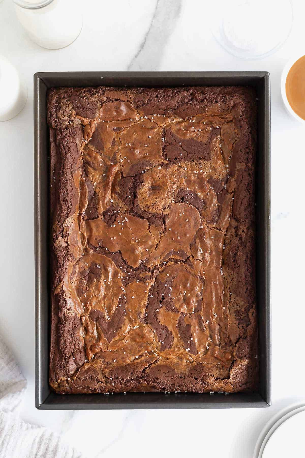 A dark baking pan of dulce de Leche Brownies on a white marble counter.