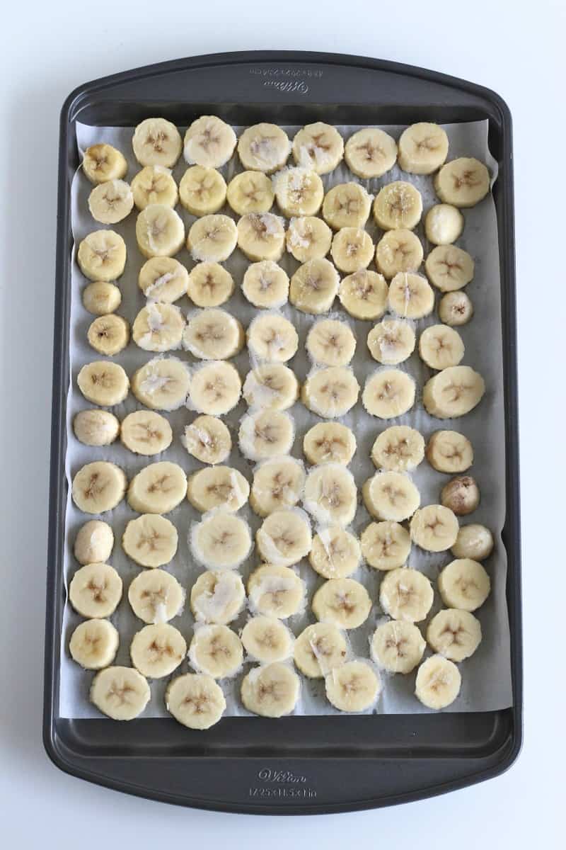 Frozen banana slices on a parchment-lined baking sheet.