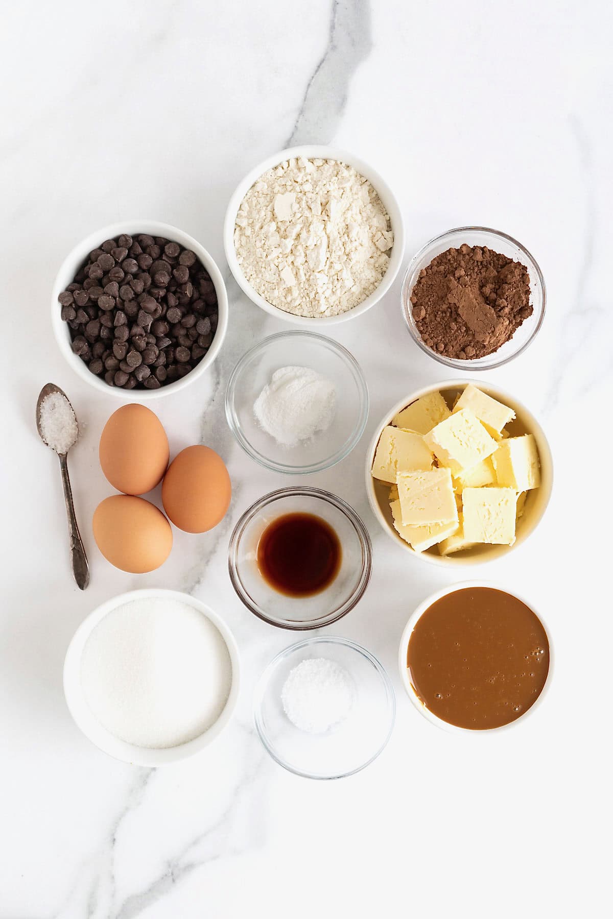 Ingredients for salted dulce de leche brownies in small glass dishes on q white marble counter.