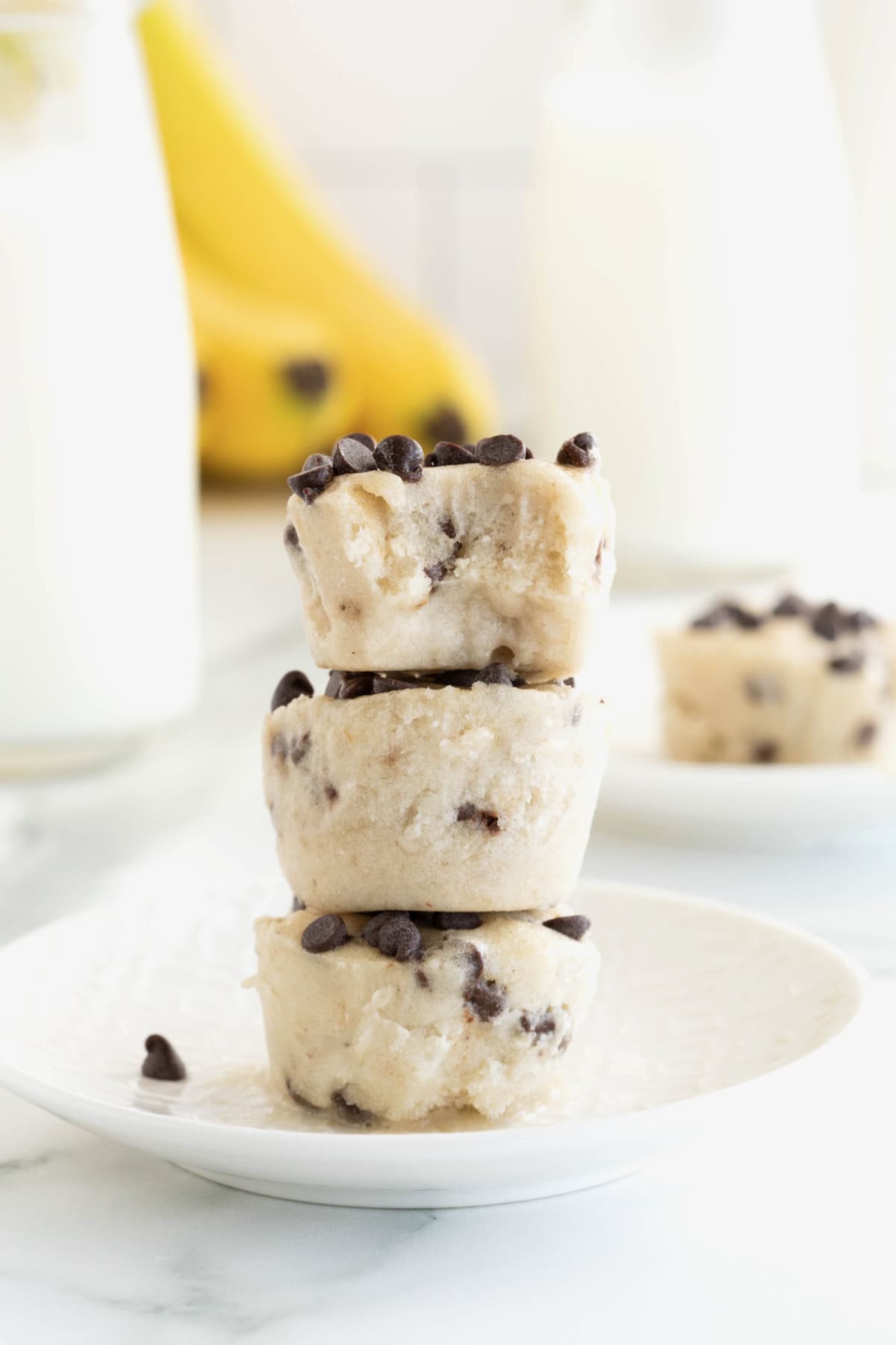 Three banana chocolate chip frozen bites stacked on a white plate.