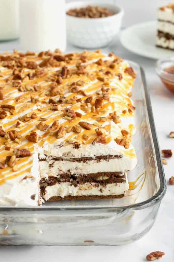 Ice cream sandwich cake topped with whipped cream, chopped pecans and a caramel drizzle in a pyrex dish.