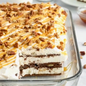 Ice cream sandwich cake topped with whipped cream, chopped pecans and a caramel drizzle in a pyrex dish.